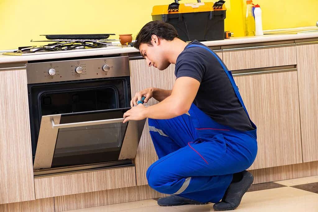 Technician crouched at an open oven door making an adjustment